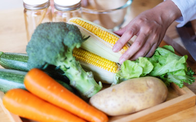 A woman chef holding and picking a fresh corn from a vegetables tray on the table