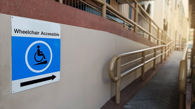 Blue Wheelchair accessible Sign and concret ramp way with handrail for support wheelchair disabled people.