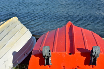 Fototapeta na wymiar Two small plastic dinghies bottom up on shore with calm water surface in background.