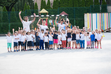 Group of children with coaches posing and waving before the lesson start. Sport school