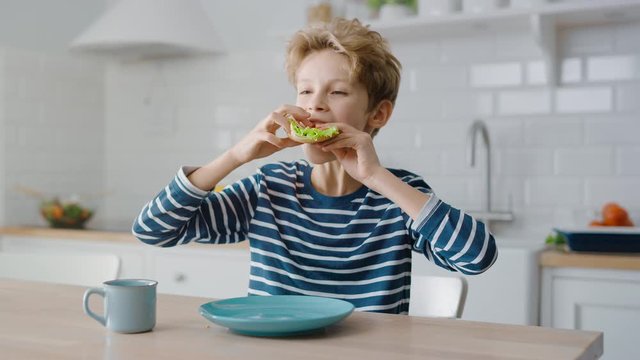 Portrait of the Cute Little Boy Eating Sandwich at the Kitchen Table. Handsome Boy Having a bite of Healthy Snack