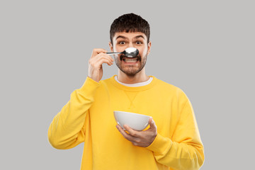 breakfast, eating and people concept - happy smiling young man with spoon and bowl having fun over grey background