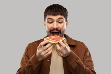 fast food and people concept - hungry young man eating pizza over grey background