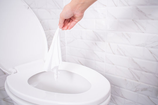 Close up hand throwing toilet paper to the toilet in a white tile bathroom