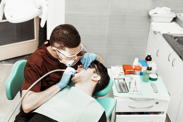 A young male dentist doctor treats a patient. Medical manipulations in dentistry, surgery. Professional uniform and equipment of a dentist. Healthcare Equipping a doctor’s workplace. Dentistry