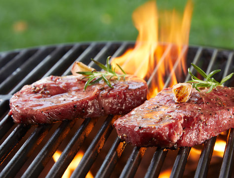Beef steak seasoned with herbs on burning grill