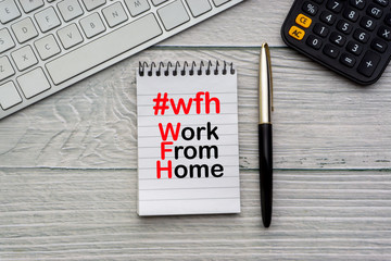 WORK FROM HOME #WFH text with notepad, keyboard, fountain pen and calculator on wooden background. Business and Healthcare concept