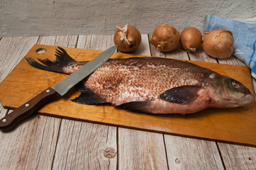 Cooking fresh river fish.Peeled fish-bream (Abramis), with onions and a knife close-up lies on a cutting board on a wooden background. Selective focus.