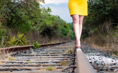 Detail of legs of a real woman walking on the railroad track, with heels, yellow dress and hat.