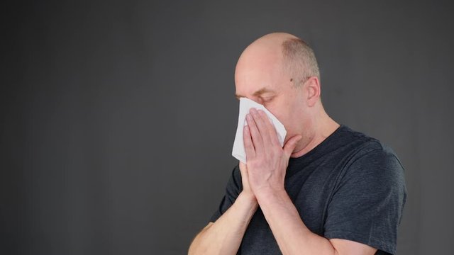 Coughing man blowing nose sneezing in white handkerchief paper napkin on black background. Cold man sneezing and blowing nose while influenza epidemic. Simptoms covid-19 concept. Seasonal allergy