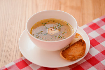 Chicken soup with vegetables and meat served in a white bowl over rustic wooden background with red plaid tablecloth.