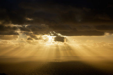 Aerial view of dark clouds back-lit by yellow evening sun over Tasman sea horizon
