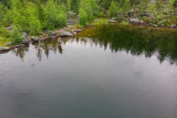 Fisherman man in mountain river in boots fly fishing salmon, morning. Aerial top view