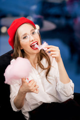 Young girl in red beret and glasses eats pink candy floss in France cafe