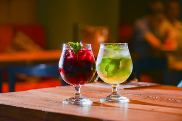 Two colorful refreshing cocktails served on a dark rustic wooden table with blurred background.