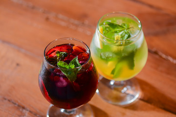 Two colorful refreshing cocktails served on a dark rustic wooden table with blurred background.