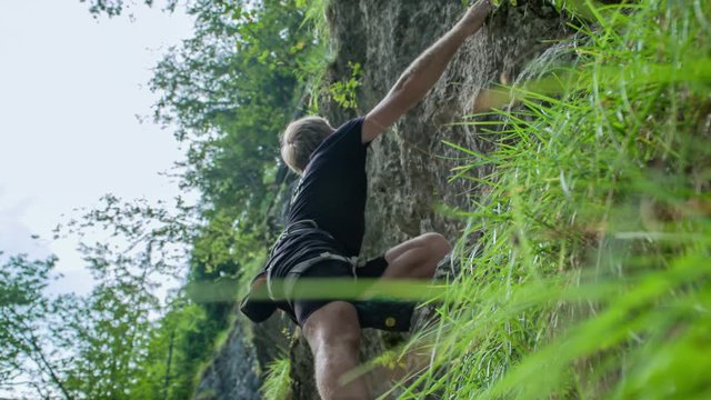 A low angle shot of a man climbing a steep mountain wall with no rope or safety equipment, just strength of his bare hands.