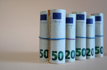 Rolls banknotes of 50 and 20 euro tied with elastic stand next to each other close up on pastel colro background