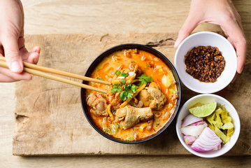 Traditional Northern Thai food (Khao Soi), spicy curry noodles soup with coconut milk and chicken in a bowl eating by using chopsticks, Top view