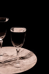 Verres à pied et assiette sur fond noir avec reflet.	