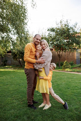 
family in nature, summer or autumn, green grass trees in green leaves, a pond in nature, mom blonde in a yellow dress, dad, husband, older son and youngest son, two children, a large and happy family