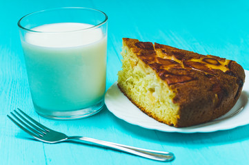 a piece of pie on a plate and a glass of milk on a blue background