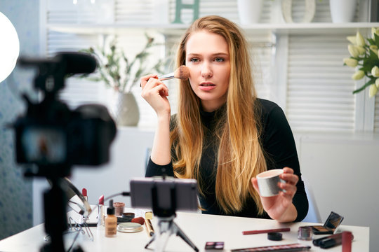 Beauty blogger woman filming daily make-up routine tutorial at camera on tripod. Influencer girl live streaming cosmetics product review in home studio. Vlogger female applies skin powder with brush. Stock Photo | Adobe Stock