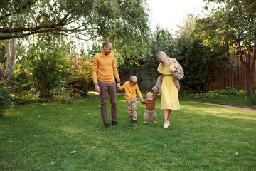 Obraz premium family in nature, summer or autumn, green grass trees in green leaves, a pond in nature, mom blonde in a yellow dress, dad, husband, older son and youngest son, two children, a large and happy family