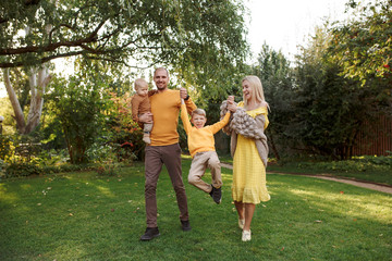 Naklejka na ściany i meble family in nature, summer or autumn, green grass trees in green leaves, a pond in nature, mom blonde in a yellow dress, dad, husband, older son and youngest son, two children, a large and happy family