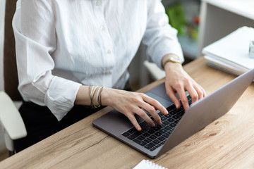 Closeup of a woman typing on laptop. Top view of female hands writing an email on keyboard on a wooden office table.