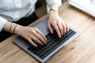Closeup of a woman typing on laptop. Top view of female hands writing an email on keyboard on a wooden office table.