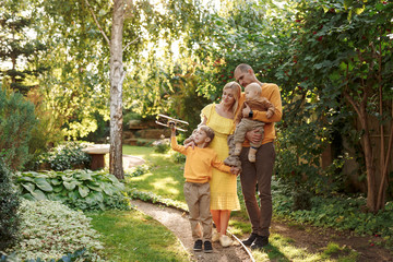 family in nature, summer or autumn, green grass trees in green leaves, a pond in nature, mom blonde in a yellow dress, dad, husband, older son and youngest son, two children, a large and happy family