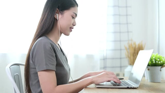 Beautiful young asian woman in grey T-shirt are working with video calling by laptop with her team for social distancing policy. Self quarantine, coronavirus, work from home concept