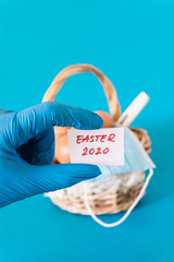 Fototapeta na wymiar Hand holding hand written sign easter 2020 in front of a basket full of eggs and protection mask