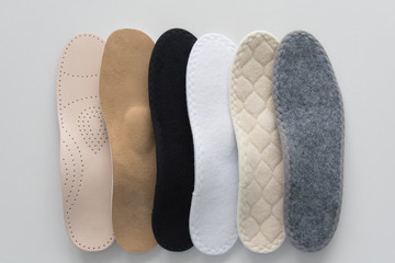 Studio photo of orthopedic insoles. A variety of orthopedic insoles are laid out in a row. Different colors and coatings: leather, cotton, microfiber.