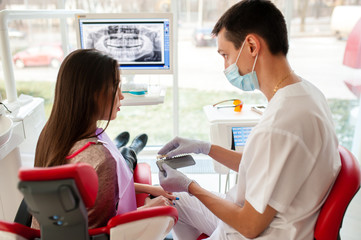 Obraz premium Choice of tooth color with a special scale. A dentist and an assistant select a shade of tooth enamel for the young pretty girl of the patient. Bleaching, prosthetics, orthopedic dentistry.