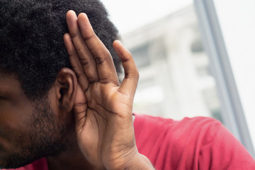 sad frustrated unhappy African black man listening ear to bad news or having hearing impair, hard of hearing; Concept of ear medication, hearing aid, rumor, fake news; African black man model
