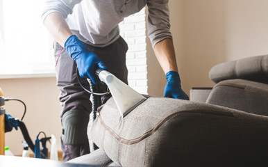 Dry cleaner's man employee removing dirt from furniture in flat, closeup, vacuum clean sofa with...