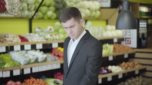 Middle shot of concentrated Caucasian man choosing pomelo in grocery. Portrait of young confident guy buying healthful food in supermarket. Healthy eating, dieting, lifestyle.