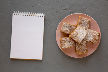 Homemade Tasty Applesauce Cake on a pink plate, blank notepad on a gray background, top view. Flat lay, overhead, from above.