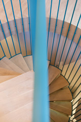 Spiral staircase, forged blue handrail and wooden steps in modern home. The view from the top.