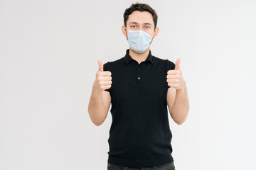 Caucasian handsome man with medical mask in black t-shirt showing thumbs up gesture and smiling, meaning well. Prevention of virus infection. Concept of Coronavirus COVID-19 Pandemic.