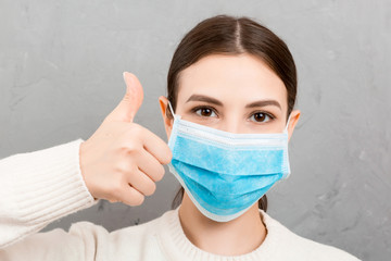 Portrait of young woman wearing medical mask at gray cement background. Person is happy because she is finally healthy. Protect your health. Coronavirus concept