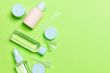Top view composition of small travelling bottles and jars for cosmetic products on green background. Facial skin care concept with copy space for your design