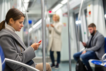 Fototapeta na wymiar Positive woman reading from mobile phone screen in metro