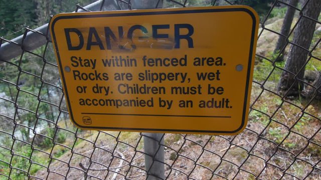 Tracking shot of danger sign attached to a fence warning about slippery rocks