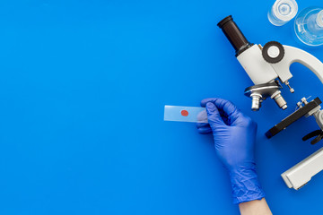 Clinical science research with microscope. Hand holds blood sample on blue background top view copy space