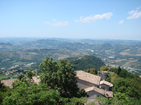 View from above of the tiled roofs of ancient houses of a small state under the rays of the summer sun surrounded by garden trees. - Powered by Adobe