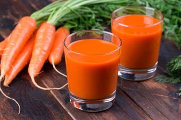 Fresh-squeezed carrot juice in glass on wooden background.