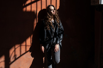 Fototapeta na wymiar Outdoor portrait of a young elegant woman in hard light with shadows of urban wearing trendy black jacket with incredible makeup. Close up. Text space.